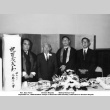 Four men standing by table, with banner in Japanese (ddr-ajah-3-189)