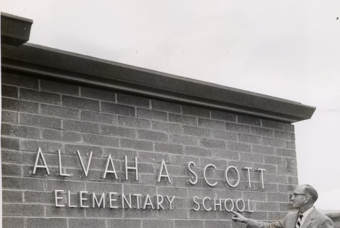 Alvah A. Scott Elementary principal pointing to the school's name plate (ddr-njpa-2-356)