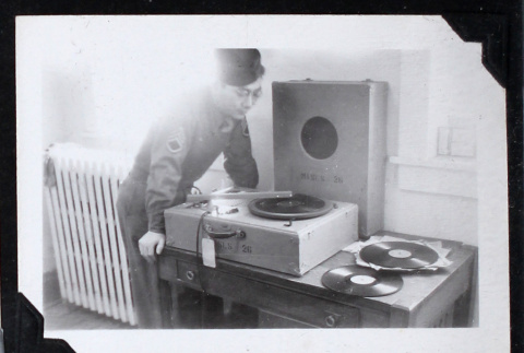 Man in military uniform leans over a record player (ddr-densho-404-86)