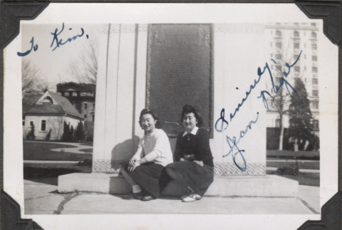 Two women sitting on curb by plaque (ddr-densho-466-218)