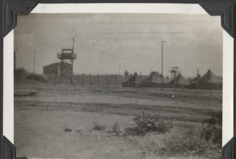View of tents behind fence and guard tower (ddr-densho-466-665)