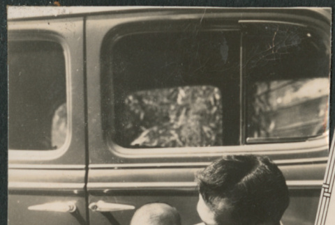 Man holding baby sitting on running board of car (ddr-densho-523-59)