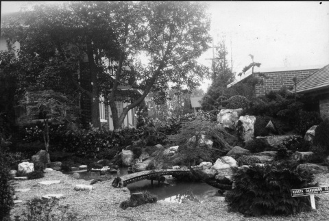 Bridge, pond, landscape and stone installation in a private garden with a Kubota Gardening Company sign (ddr-densho-354-113)