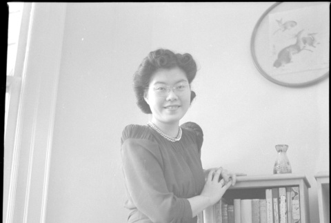 Tomoye (Nozawa) Takahashi standing by bookshelf (ddr-densho-426-2025)