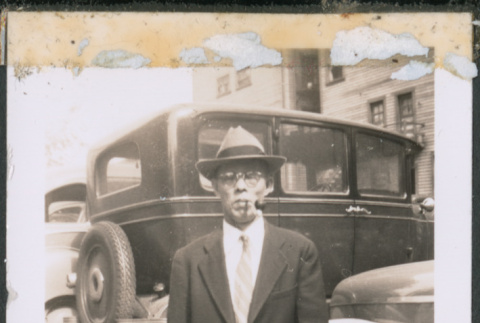 Man with glasses carrying a bag standing by row of cars (ddr-densho-483-993)