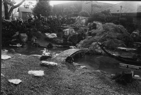 Bridge over pond in a private garden with a Kubota Gardening Company sign (ddr-densho-354-114)