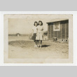 Nisei women standing outside with barracks in the background (ddr-csujad-44-7)