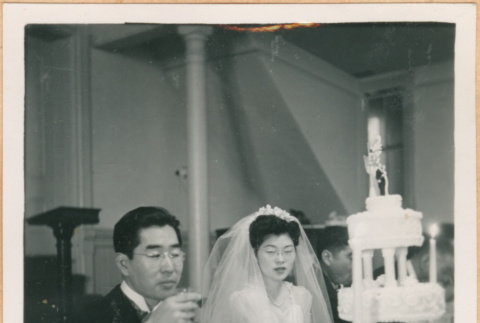 Henri Takahashi and Tomoye (Nozawa) Takahashi seated at head table with wedding cake (ddr-densho-410-494)