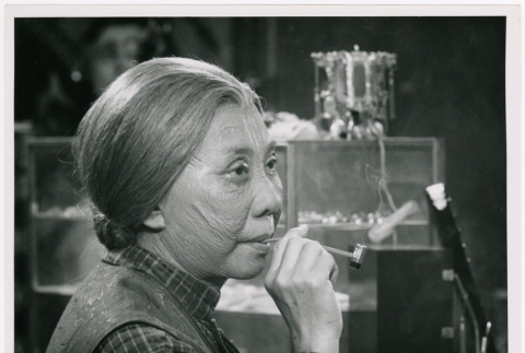 Mary Mon Toy profile holding pipe on set of Kojak episode (ddr-densho-367-362)