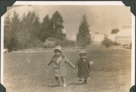 Two children running across field holding hands (ddr-densho-483-545)