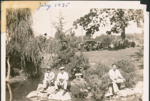 Three men sitting on rocks next to pond in Japanese Garden (ddr-densho-483-559)