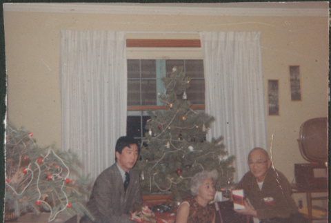 Chester and Agnes Sakura with man by Christmas tree holding presents (ddr-densho-523-468)