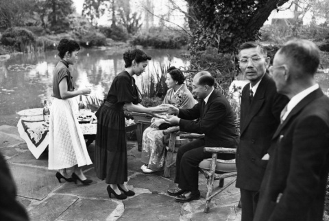 Women serving drinks to seated couple in garden (ddr-ajah-3-28)