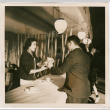 Woman handing package to man across counter (ddr-densho-426-1873)