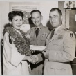 Woman wearing leis receiving a check from two men in military dress (ddr-njpa-2-368)