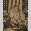 Man wearing leis reading speech in front of flags (ddr-njpa-2-871)