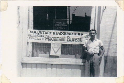 James Omura standing before Voluntary Headquarters, Pacific Coast Evacuee Placement Bureau (ddr-densho-122-684)