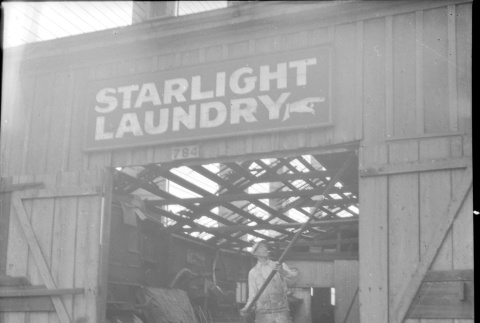Man working on demolition of building with Starlight Laundry sign over door (ddr-densho-426-2161)