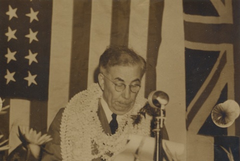 Man wearing leis reading speech in front of flags (ddr-njpa-2-871)