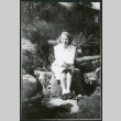 Photograph of Dr. Agnes V. Barlett sitting on a rock in front of the Manzanar hospital (ddr-csujad-47-321)
