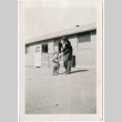 Sally Domoto walking with toddler outside barracks (ddr-densho-329-1340)