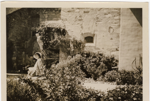 Tomoye (Nozawa) Takahashi sitting in garden by stone building (ddr-densho-426-1785)