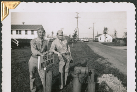 Two men leaning on sign by fire hydrant (ddr-densho-434-374)