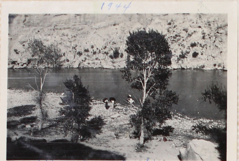 View of river from hill, two people standing on river's edge (ddr-densho-464-49)
