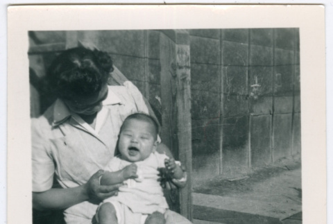 Woman holding baby, sitting on barracks steps in Minidoka (ddr-densho-543-4)