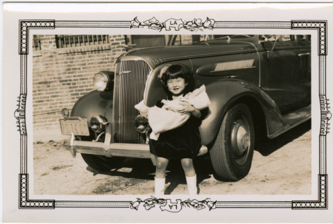 Girl holding doll standing in front of car (ddr-densho-426-1927)