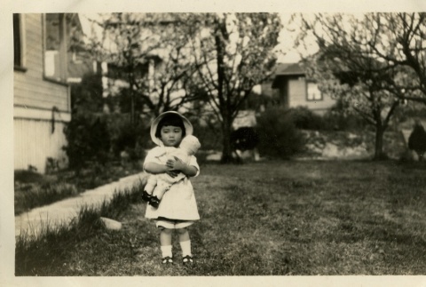 Nisei girl with doll in backyard of house (ddr-densho-182-154)