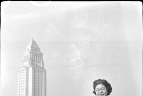Tomoye (Nozawa) Takahashi standing with large building in background (ddr-densho-426-1764)