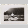 Yuri Tsukada sitting on river rock (ddr-densho-356-142)