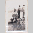 Three men standing on log along shore, one facing camera (ddr-densho-464-86)