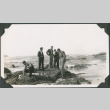 Group of men in civilian clothes standing on rocks by shore (ddr-ajah-2-126)