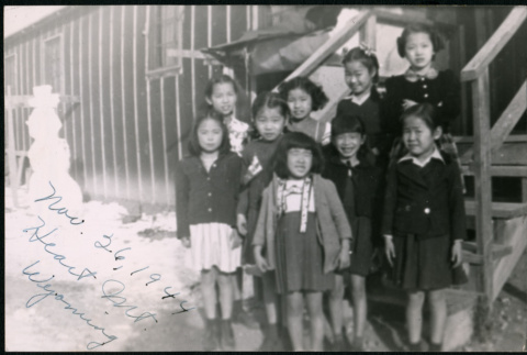 Nine young Japanese American girls take group photo near camp barracks steps (ddr-densho-362-38)