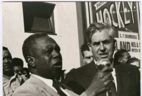 Two men speaking at a microphone by crowd (ddr-densho-426-982)
