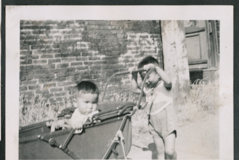 Photo of a child in a pram being pushed by another child (ddr-densho-483-789)