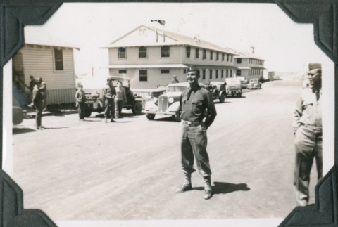 Man in uniform standing in road with buildings and ground of men in background (ddr-ajah-2-43)