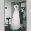 Bridesmaid removing wedding dress from hanger (ddr-densho-523-347)