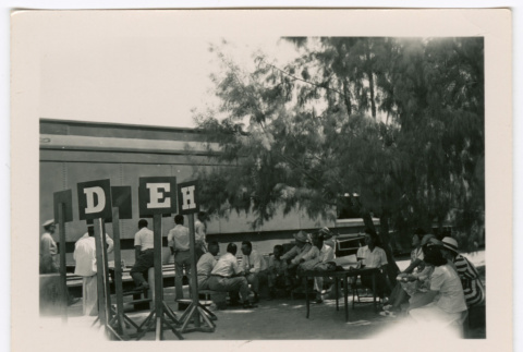 Group waiting at tables with train in background (ddr-densho-475-396)
