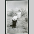 Photograph of two women standing and sitting on a gate at Manzanar (ddr-csujad-47-182)