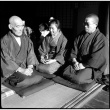 Two men and a woman seated in doorway of house (ddr-densho-426-312)