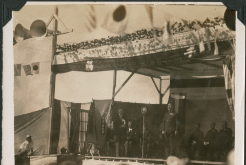 Man speaking on stage, with row of men behind him (ddr-densho-483-526)
