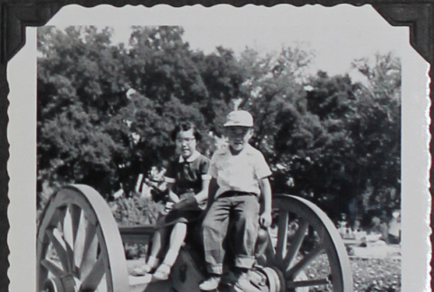 Two children sitting on cannon wheels at Sutter's Fort (ddr-densho-300-599)