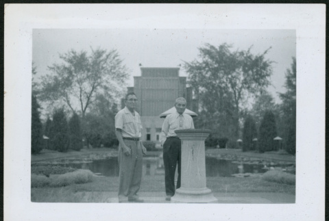 Two men standing by pillar and pond (ddr-densho-293-182)