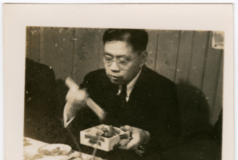Man serving himself food from a dish with chopsticks (ddr-densho-426-1736)