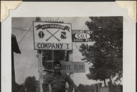 Man standing under sign for 442nd Infantry Company I (ddr-densho-466-869)