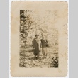 Photograph of two people standing in a field surrounded by trees (ddr-densho-329-408)