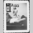 Man laying on cot looking at pictures of women (ddr-densho-434-421)